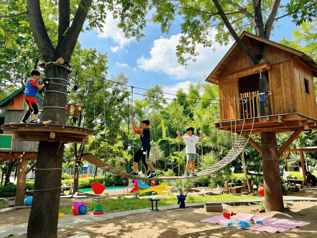 Children joyfully crossing a rope bridge surrounded by treehouses and greenery, capturing playful outdoor adventure.