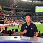 Sports journalist reporting kora live news in a vibrant stadium with cheering fans.